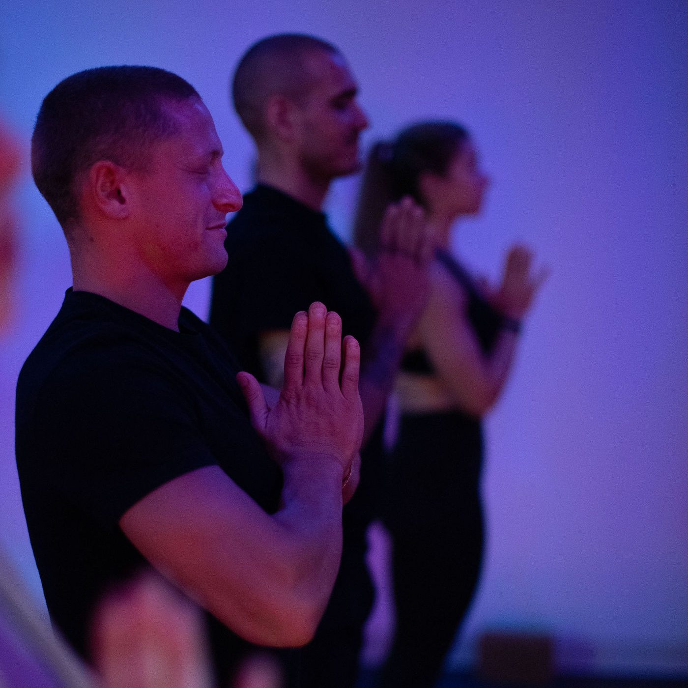 yoga pod students standing in a line with hands at heart center under purple studio light